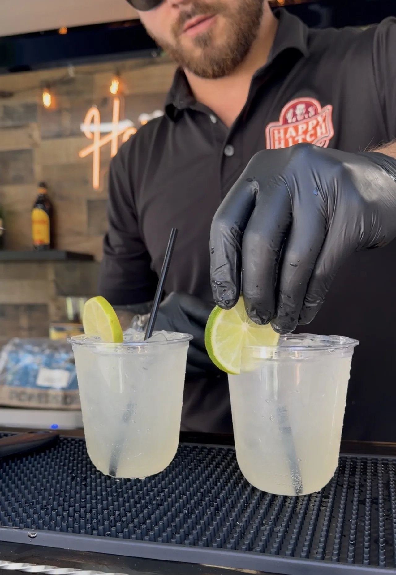 A Happy Hitch bartender in a branded shirt garnishing two iced drinks with lime slices