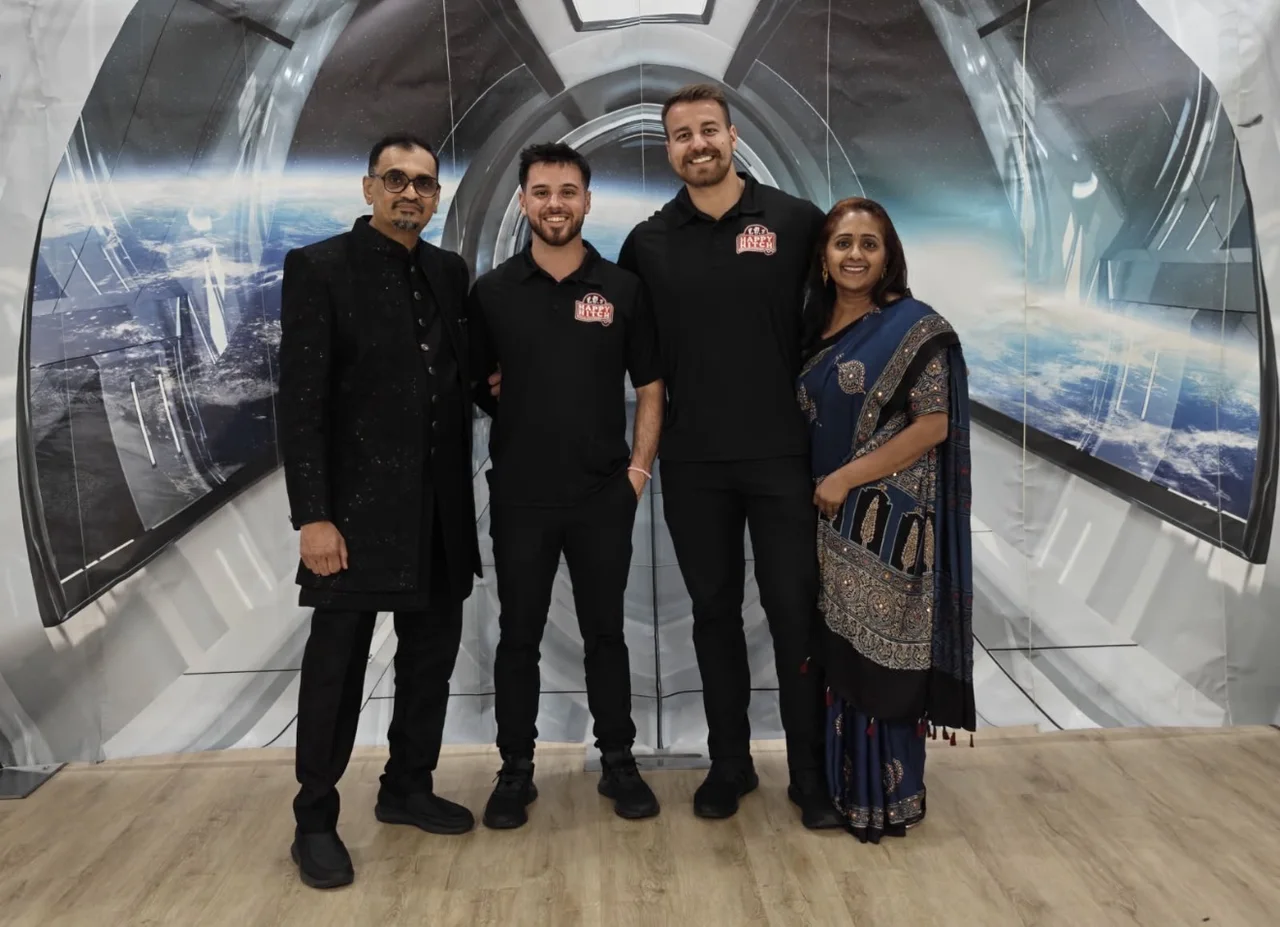 Two Happy Hitch bartenders in branded black shirts posing with two guests in front of an indoor backdrop