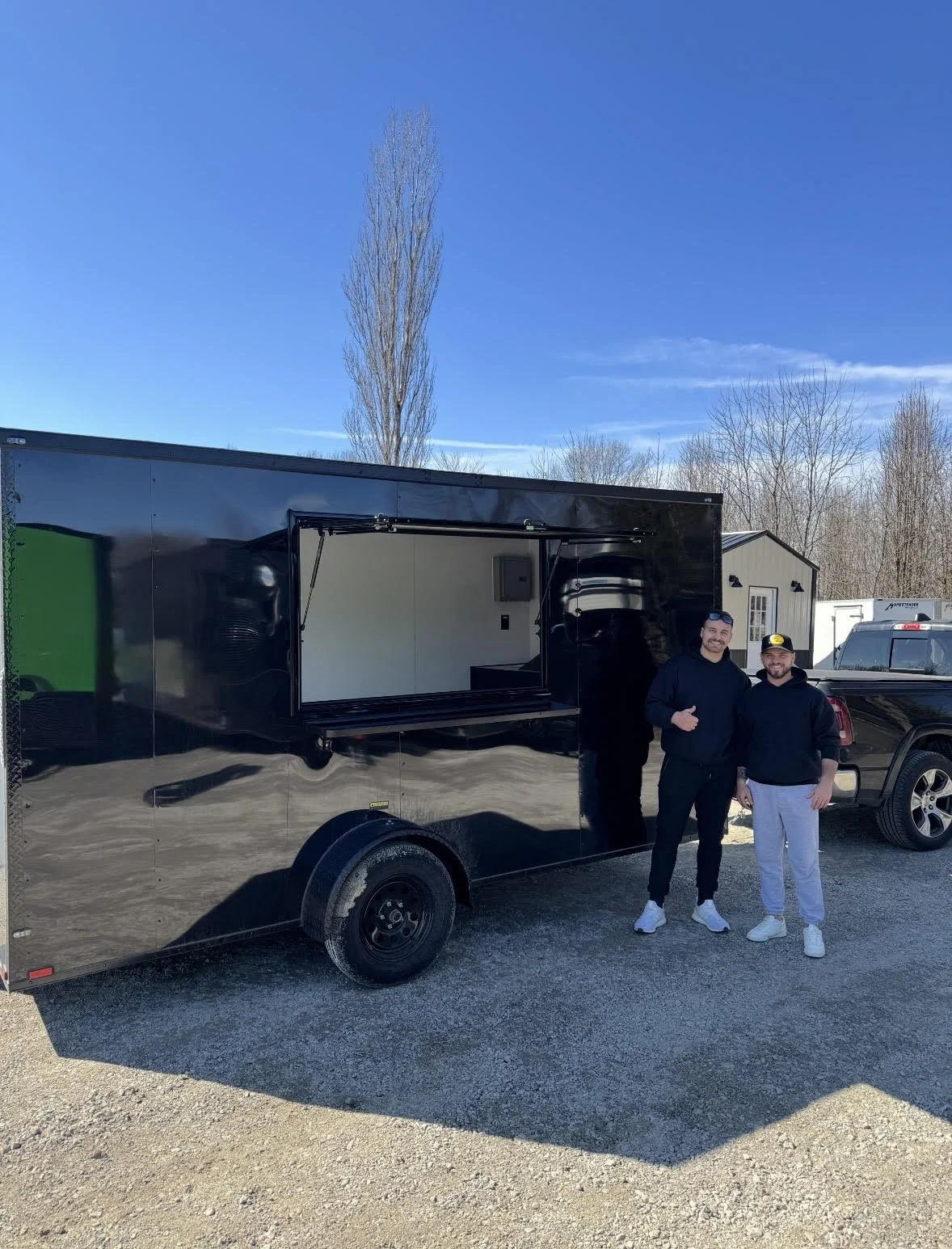 Jake and Dillon standing beside the black Happy Hitch trailer with its service hatch open on a sunny day